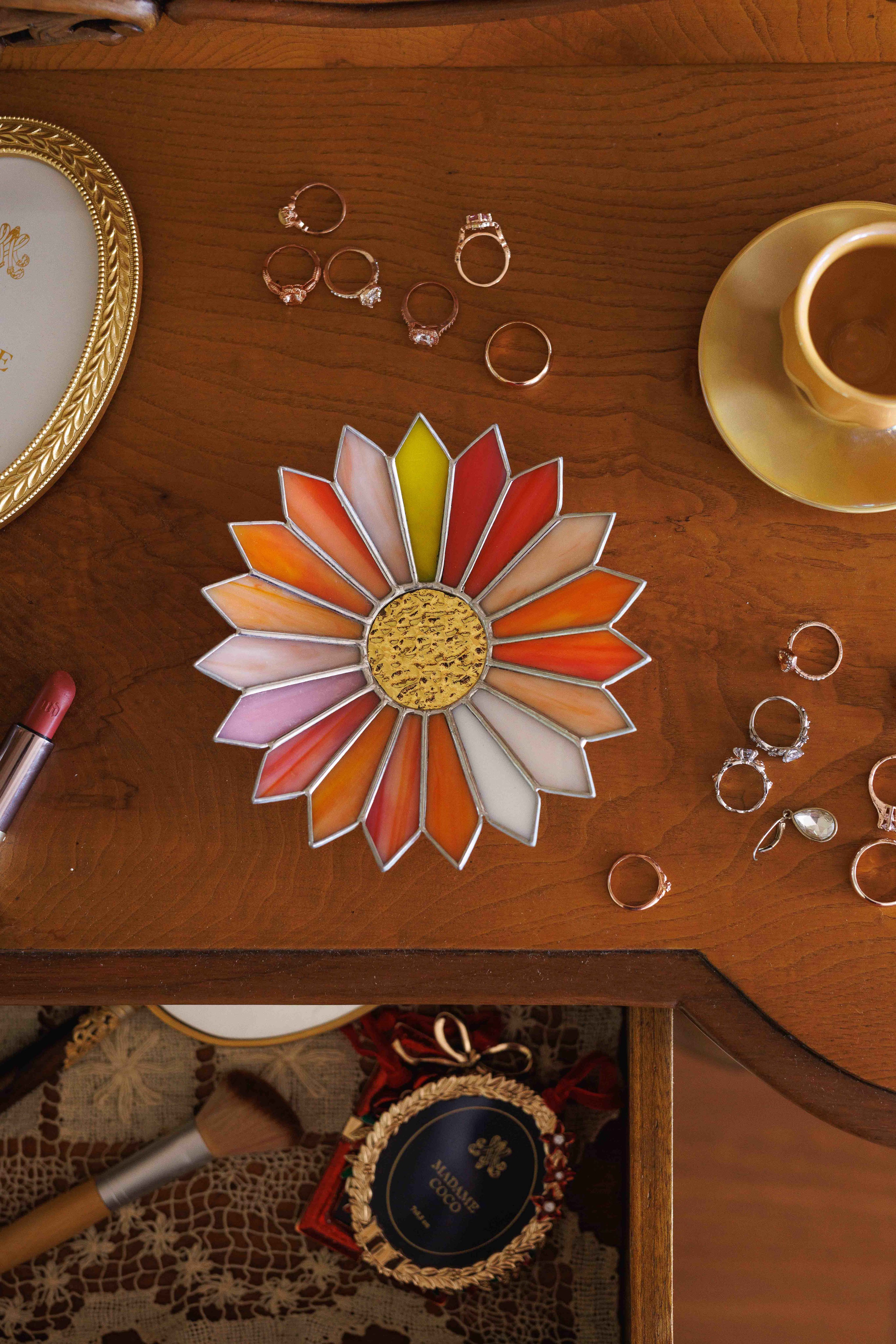 stained glass sunburst jewelry tray on vintage wooden vanity table with rings, lipstick and coffee cup, warm aesthetic jewelry holder