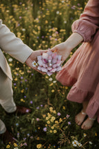 Two people holding hands with a pink flower shaped engagement ring holder against a floral background