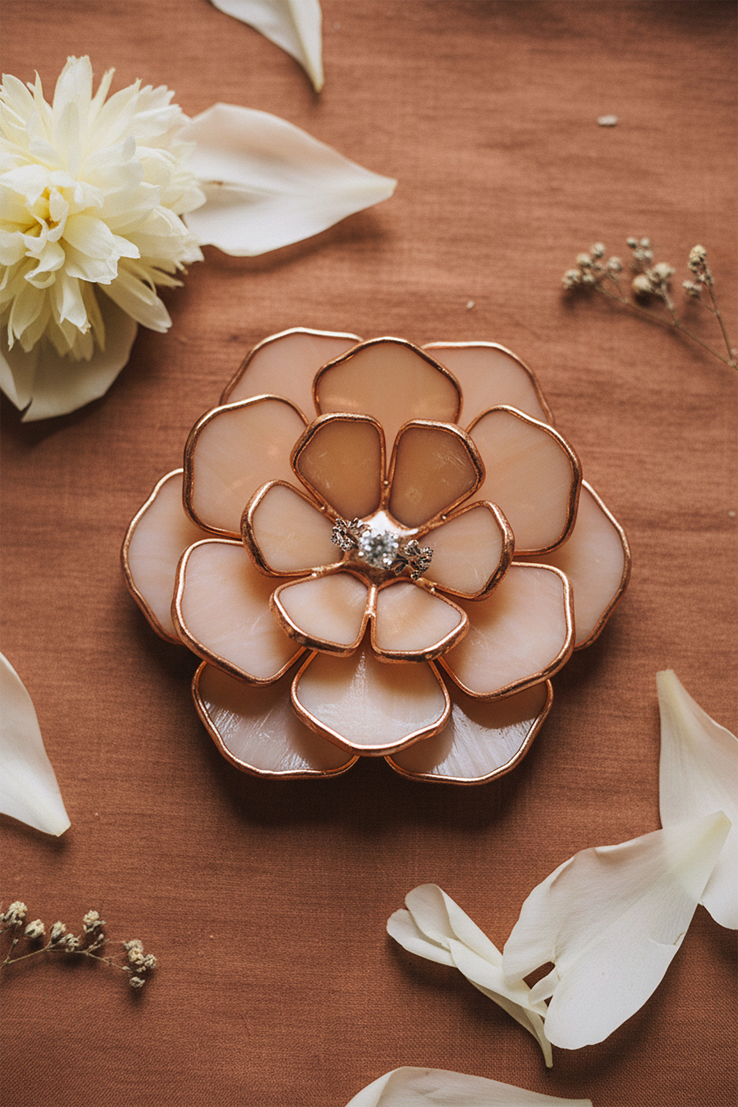 Decorative peony-shaped wedding ring holder with a central gemstone on a wooden surface with white flowers.
