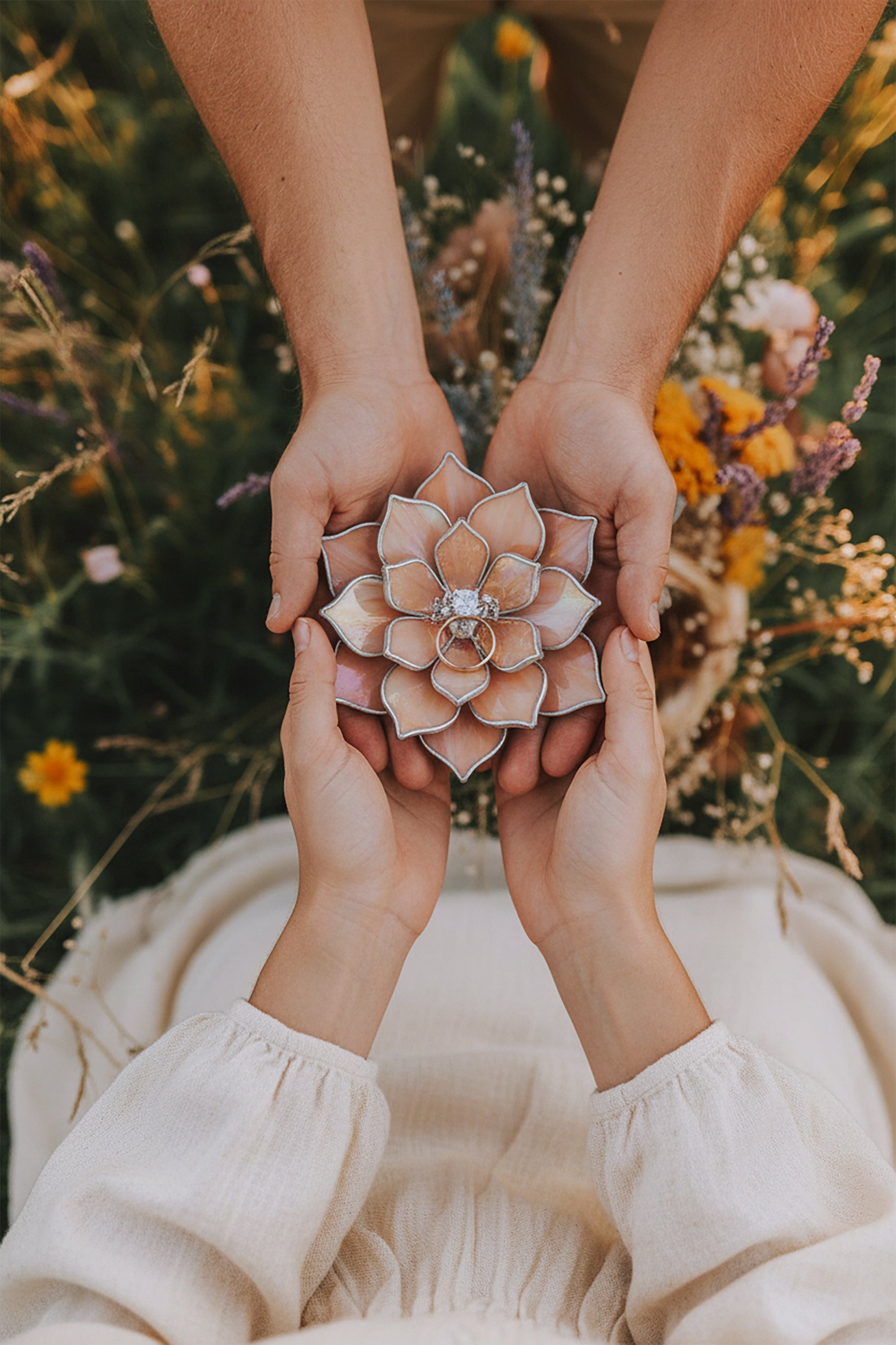 Hands holding a pink flower engagement ring dish against a natural background with flowers.