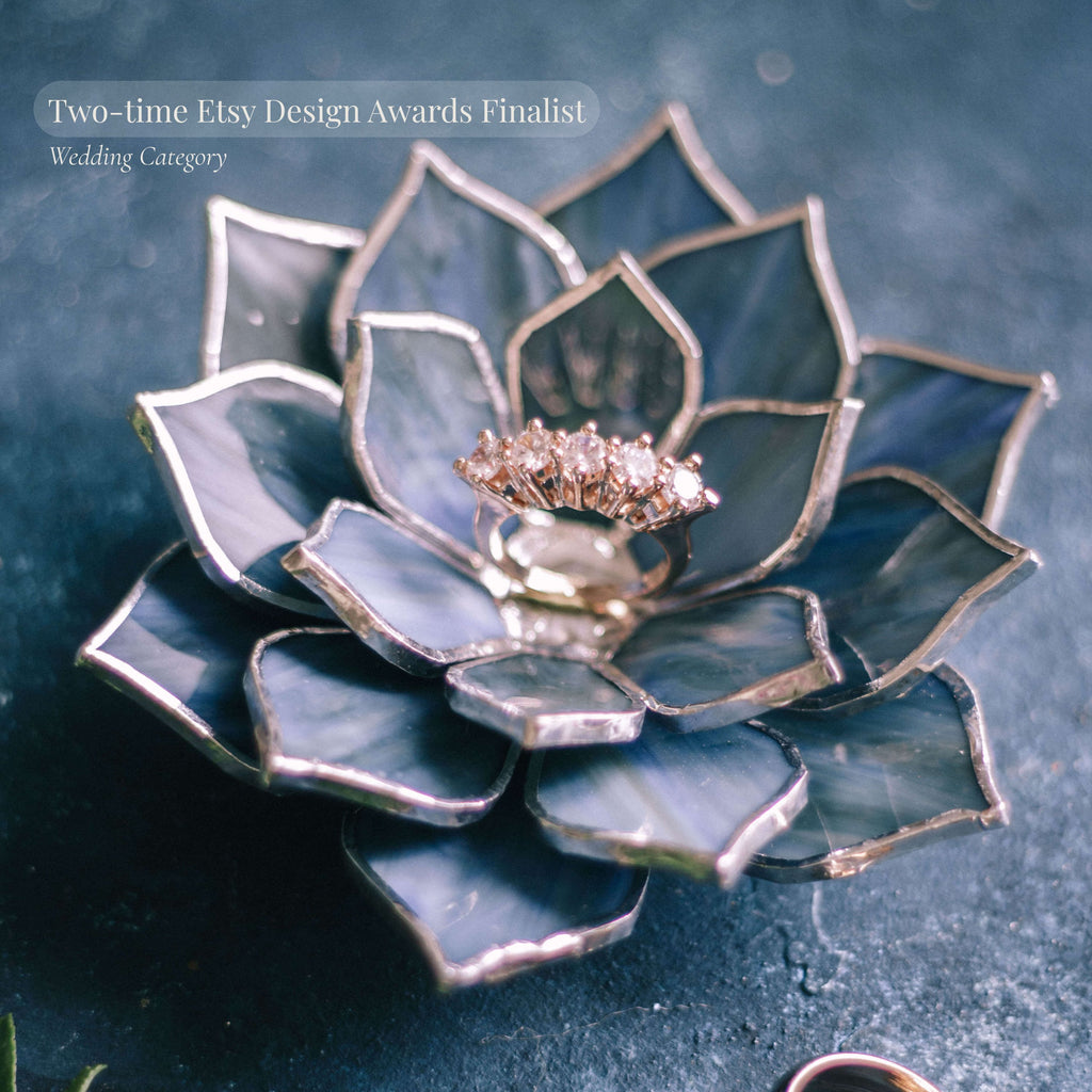 Award-winning handmade stained glass succulent ring dish in deep blue tones with metallic edging, holding a diamond ring at the center; two-time Etsy Design Awards finalist in wedding category, premium ring holder for engagement display, ceremony styling, and luxury gift for bride or couple.