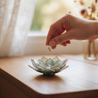 Hand placing delicate gold earrings into a handmade stained glass succulent jewelry dish in sage green and soft mint tones with silver edges; decorative ring and earring holder on wooden surface by window light, ideal for vanity organization, everyday jewelry storage, home decor accent, and thoughtful gift for her.